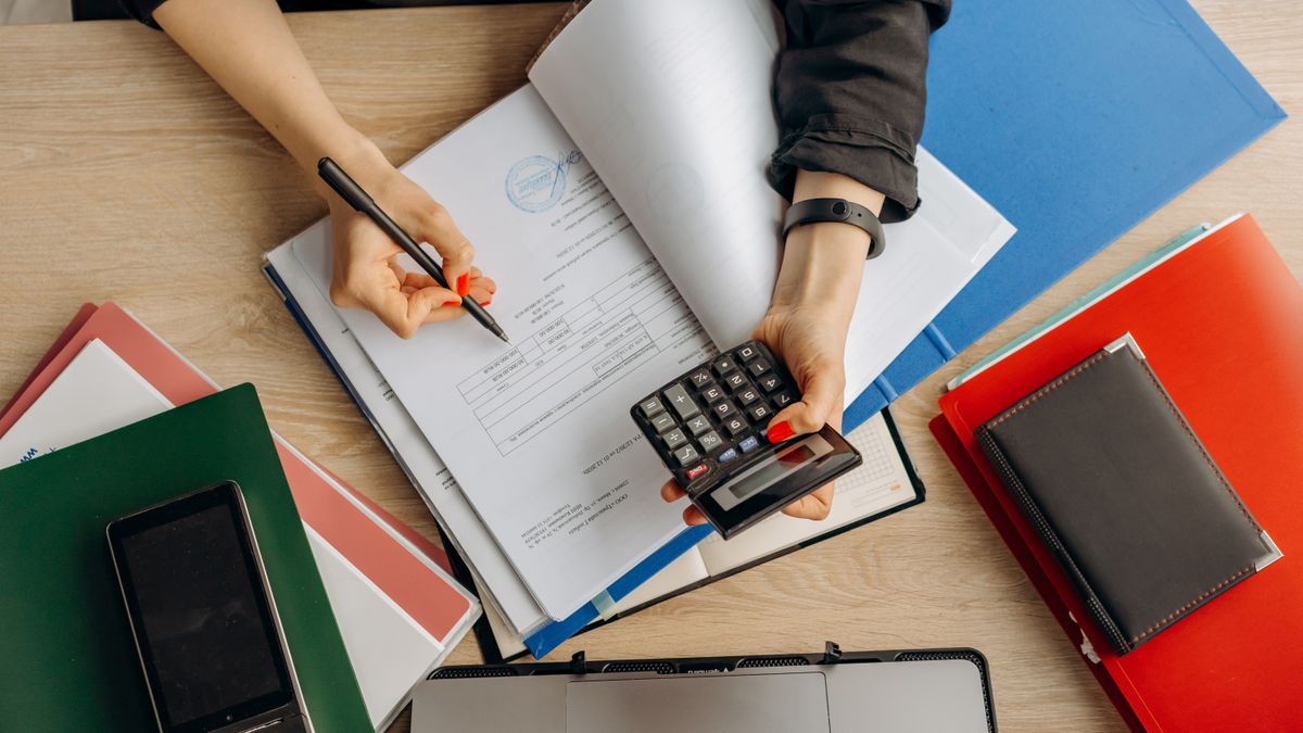 Hands reviewing financial documents beside a calculator.